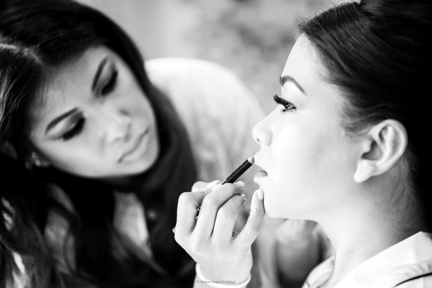 Black and white photo of a makeup artist applying lipstick to a young woman client.