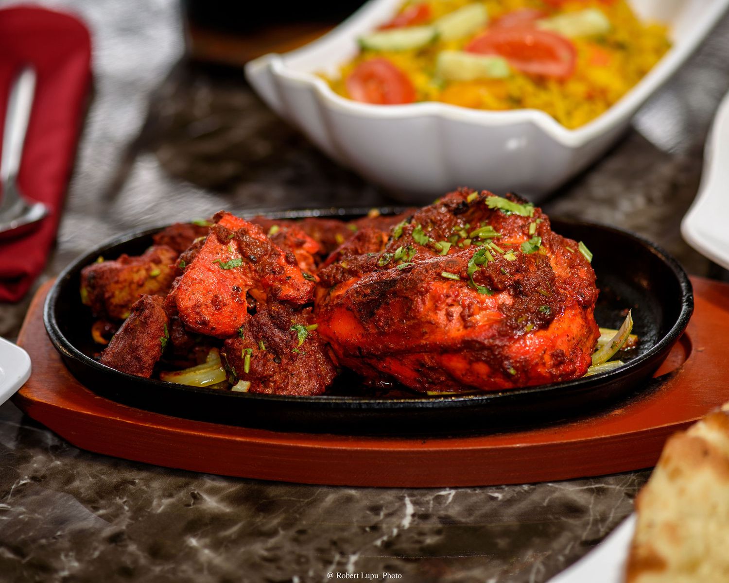 Sizzling tandoori chicken served on a cast iron plate with fresh herbs and vegetables at an Indian restaurant.