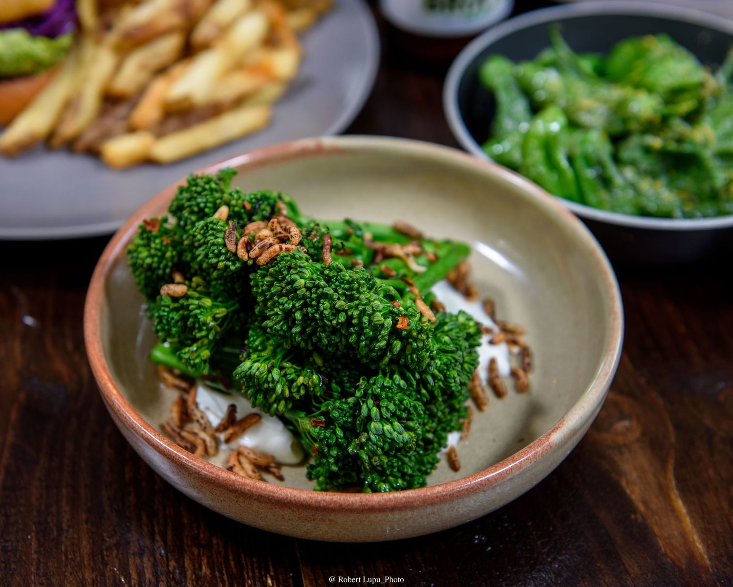Fresh steamed broccoli florets topped with toasted garlic in a rustic ceramic bowl on a wooden table.