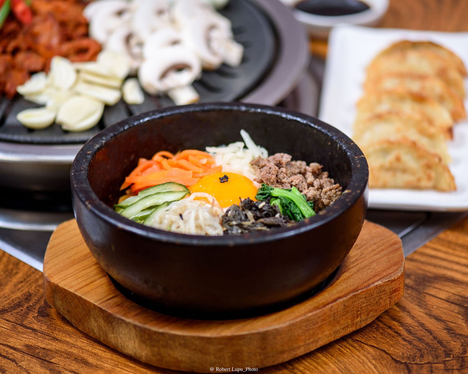 Korean bibimbap served in a hot stone bowl with colorful vegetables, egg, and meat on a wooden board.