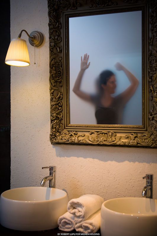 Elegant bathroom with ornate gold mirror reflecting silhouette, two round vessel sinks, and vintage wall sconce lighting.