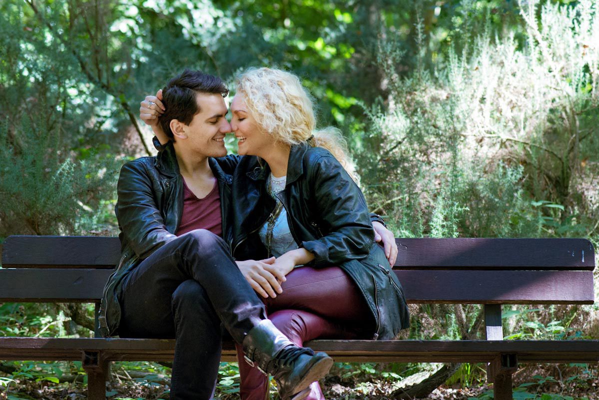 Two women sitting close on a park bench, smiling and sharing an intimate moment outdoors.