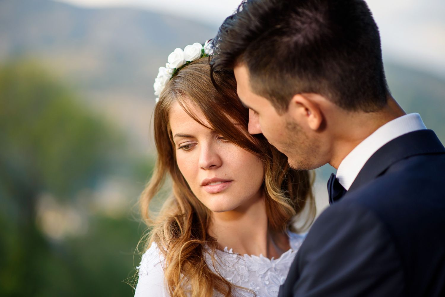 Beautiful bride wearing floral crown sharing intimate moment with groom outdoors on wedding day.