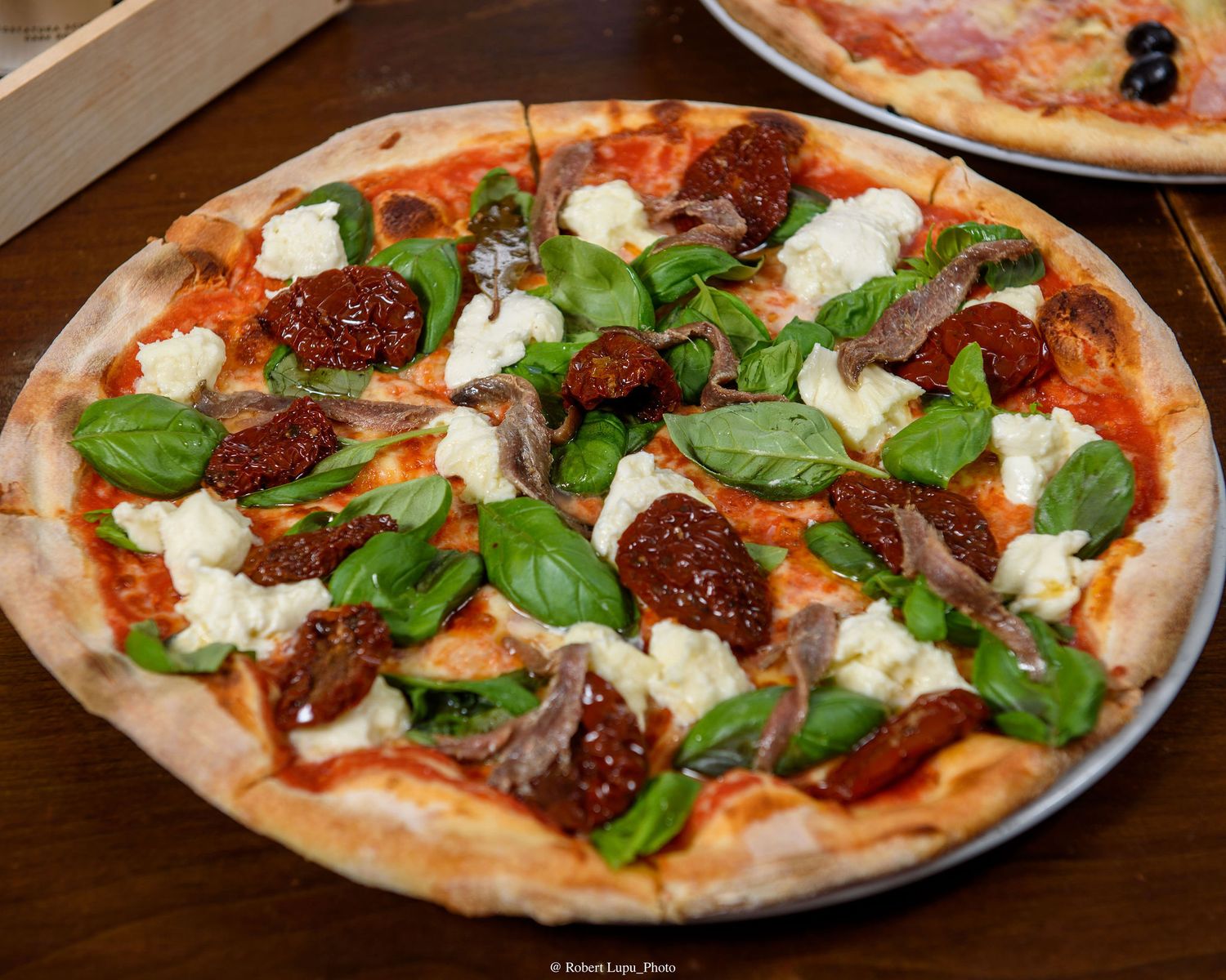 Neapolitan pizza topped with sun-dried tomatoes, fresh mozzarella, basil leaves, and cured meat on tomato sauce.