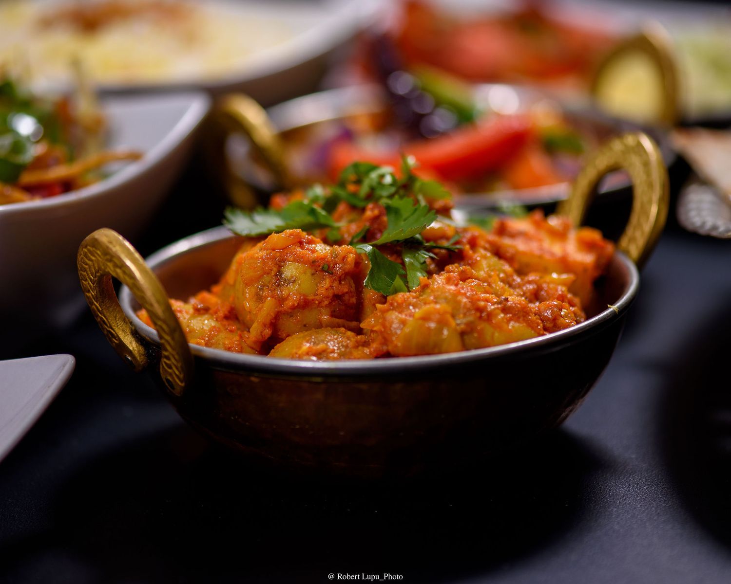 A rich and spicy Indian curry served in a traditional copper kadai bowl, garnished with fresh cilantro.