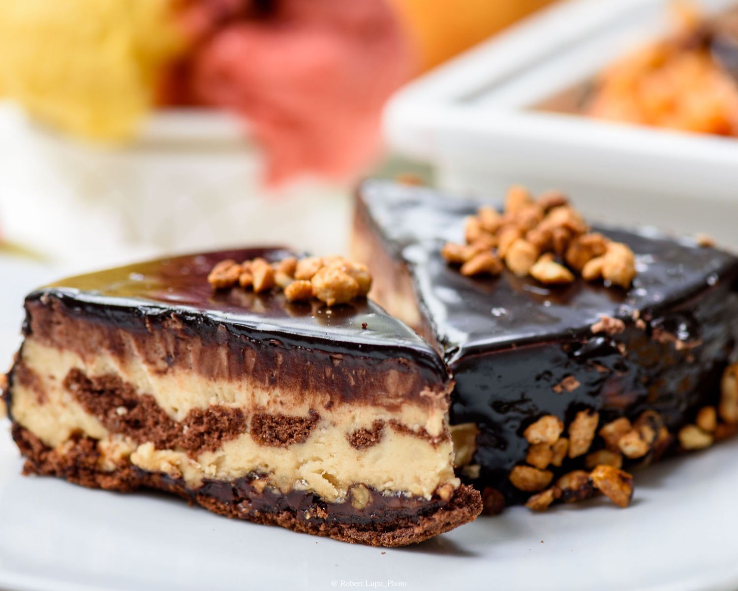 Decadent chocolate ganache layered dessert bar with peanut butter filling and walnut topping on a white plate.