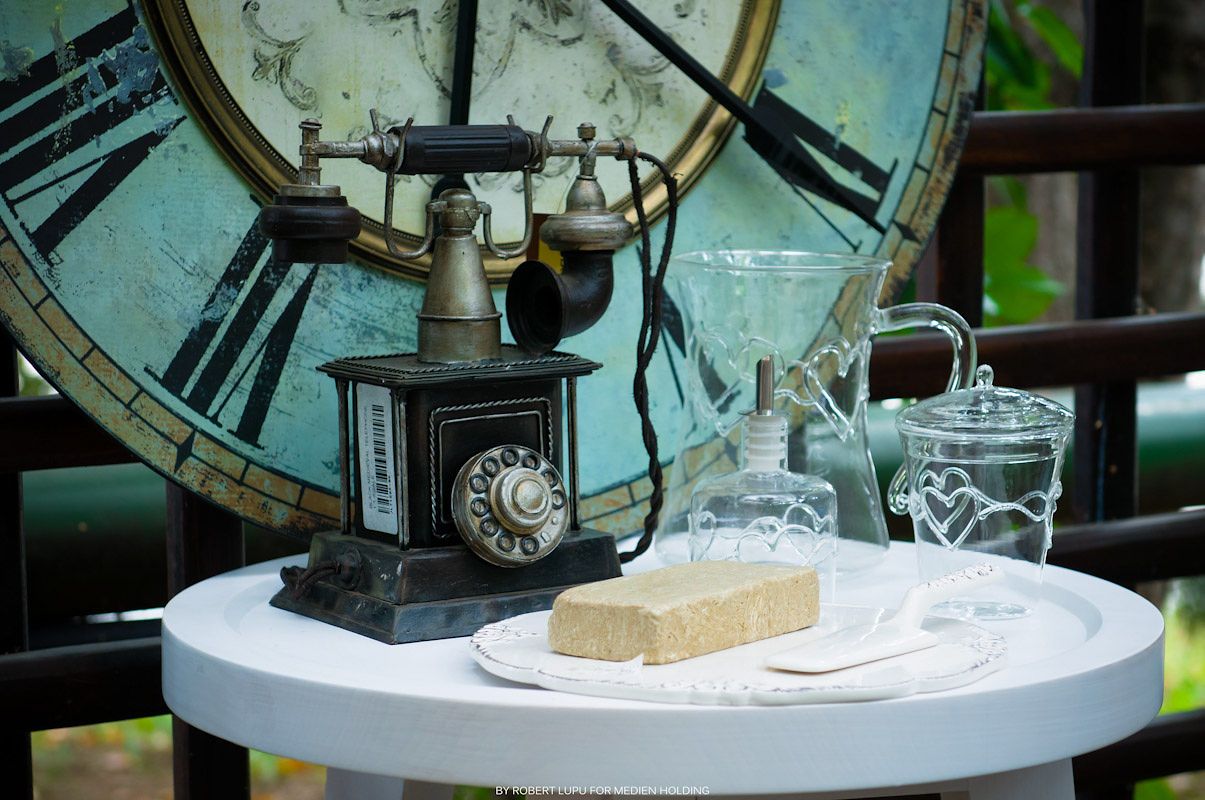 Vintage rotary telephone beside antique glass bottles on a white table with a large ornate clock in the background.