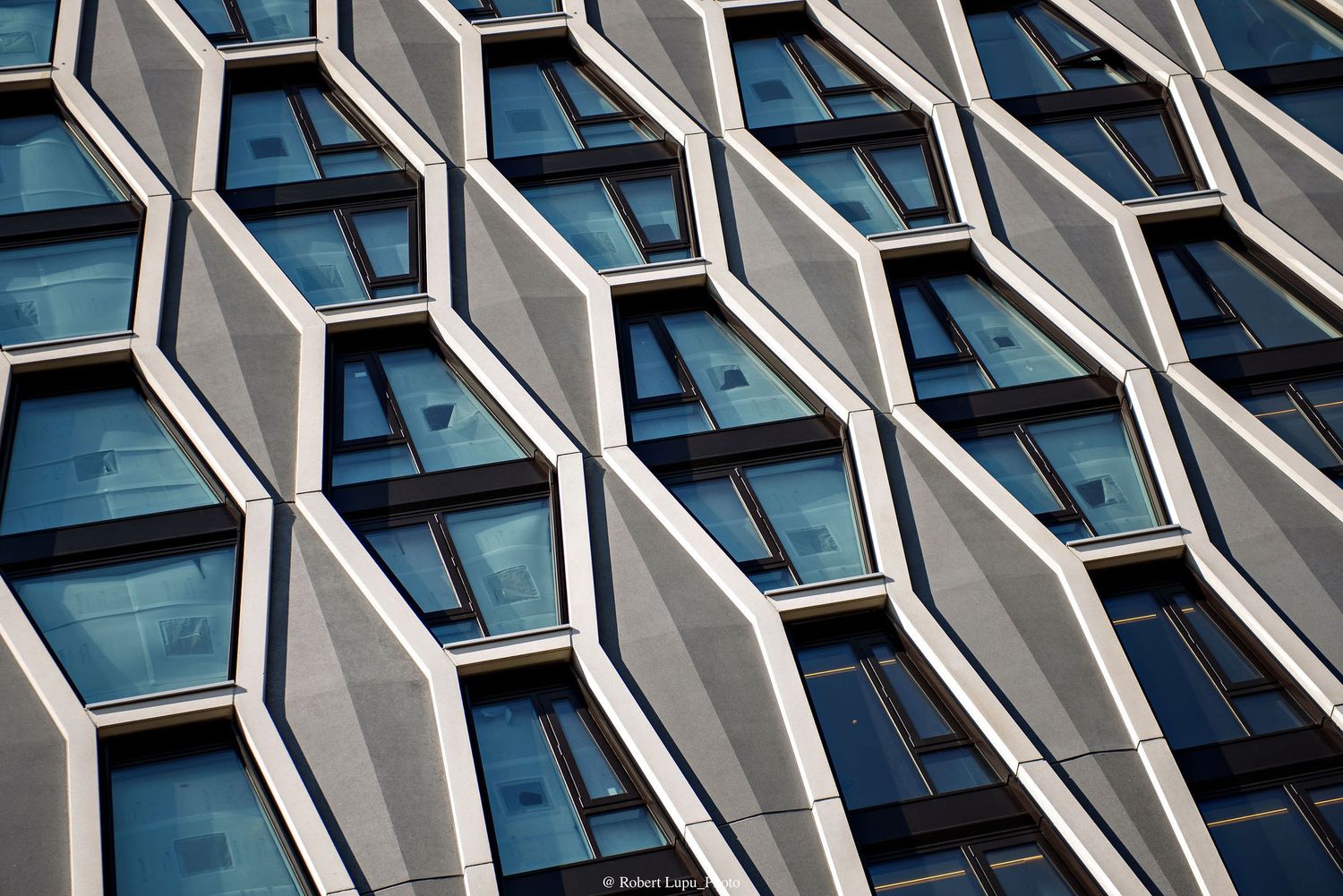 Modern building facade with geometric hexagonal windows in a repeating pattern, reflecting blue sky on glass panes.