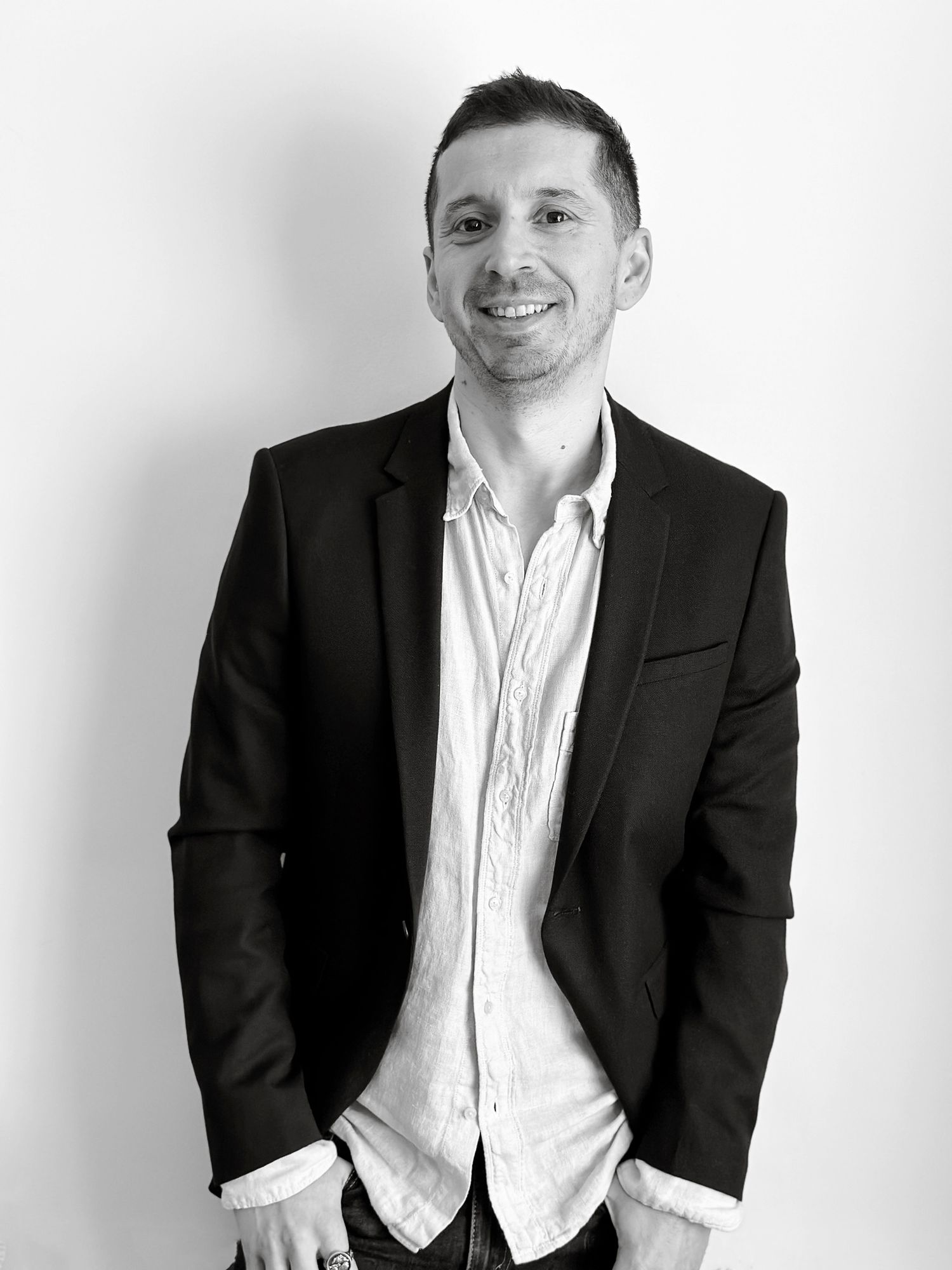 A smiling man in a black blazer and white shirt poses confidently in a professional black and white portrait photo.