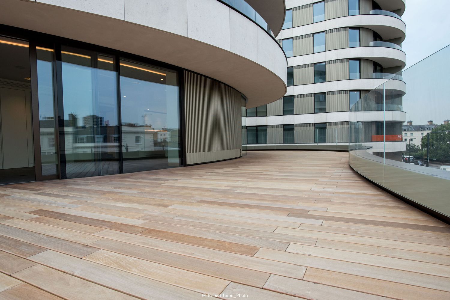 Modern rooftop terrace with wooden deck flooring on a curved contemporary building with glass sliding doors.