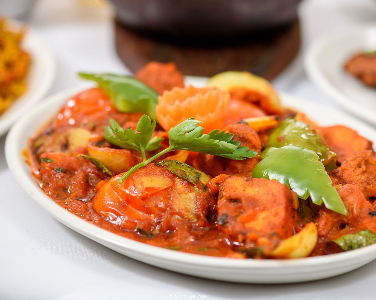 Spicy Indian curry dish with tomatoes, vegetables, and fresh cilantro garnish served on a white oval plate.