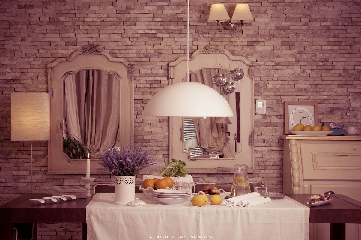 Elegant dining table with fresh fruit under pendant light, framed mirror, and lavender bouquet against rustic brick wall.