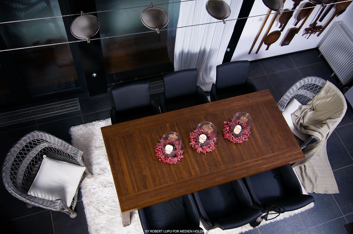 Aerial view of a modern dining room with a wooden table, red floral centerpieces, black chairs, and a white shag rug.