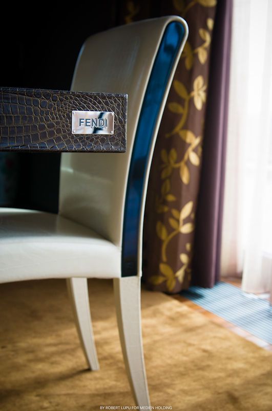 Luxury Fendi branded chair with crocodile texture back and blue accent against floral curtains.