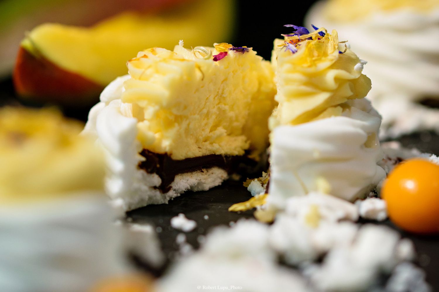 Close-up of a sliced cupcake with yellow frosting, whipped cream, and an Oreo base on a dark surface.