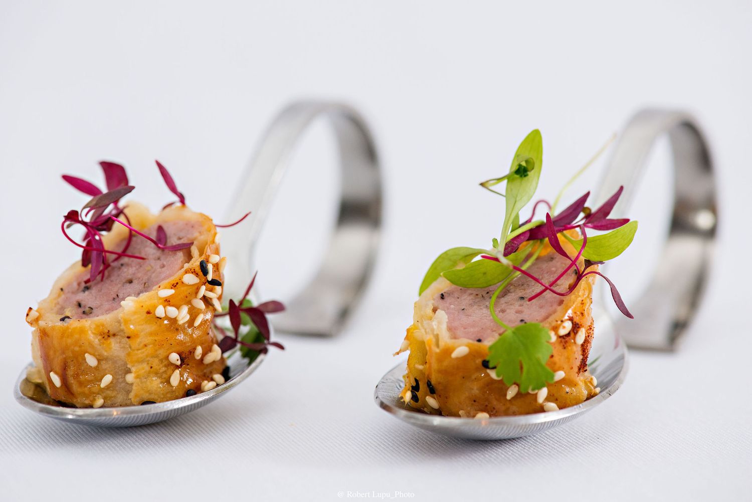 Two elegant appetizer spoons with tuna tartare, sesame seeds, and colorful microgreens on a white background.