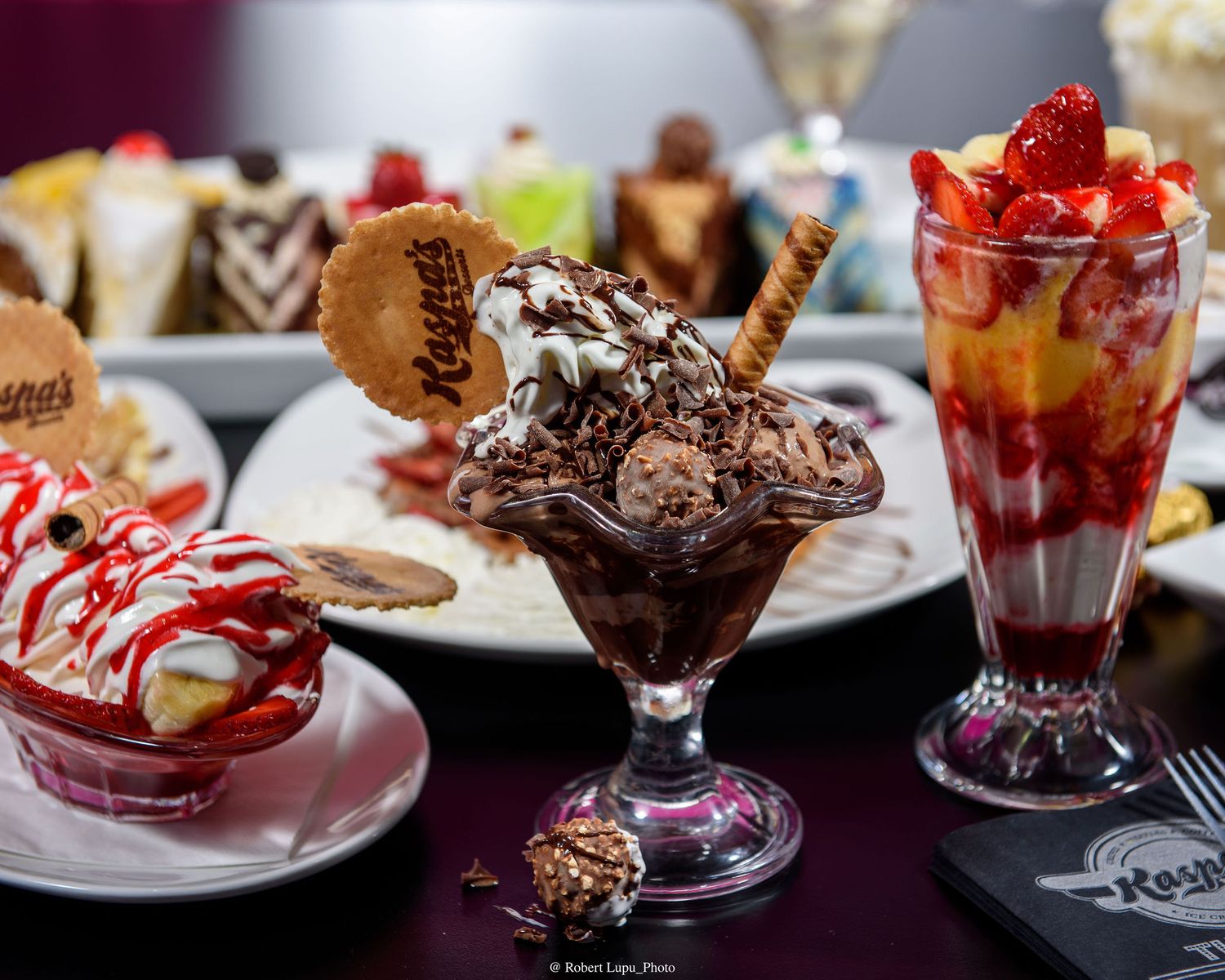 Decadent ice cream sundaes with chocolate, strawberry toppings, wafers, and cookies displayed on a dessert table.