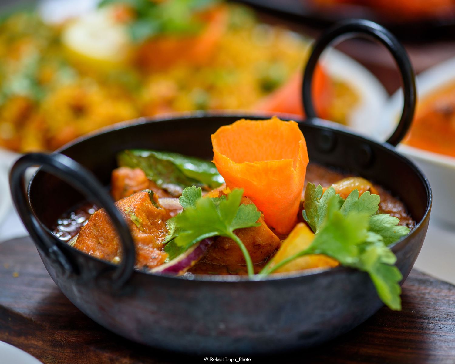 Indian curry served in a traditional black karahi with carrots, peppers, and fresh cilantro garnish.