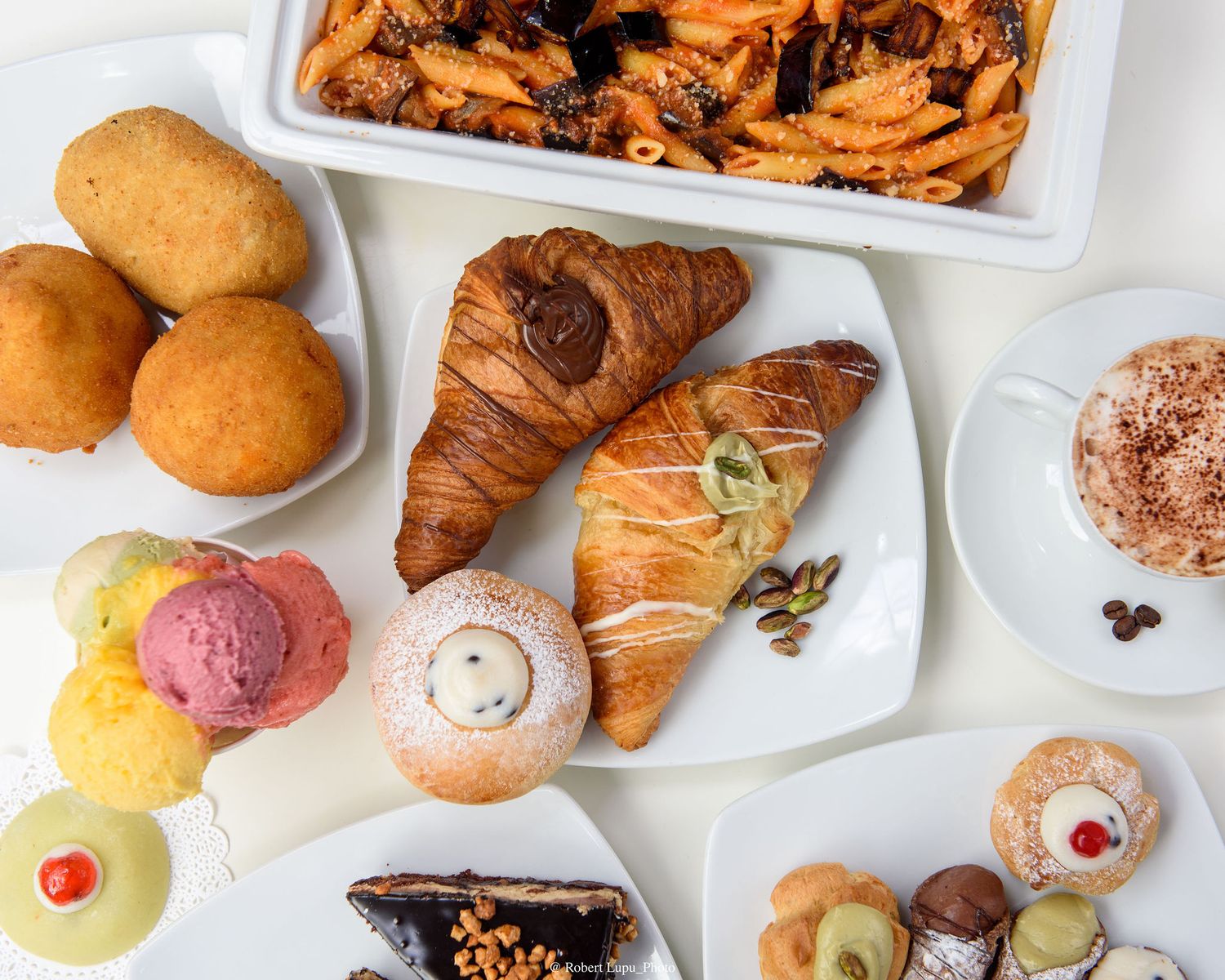 Assorted Italian pastries, croissants, fried dough, colorful gelato scoops, and baked pasta on a white table.