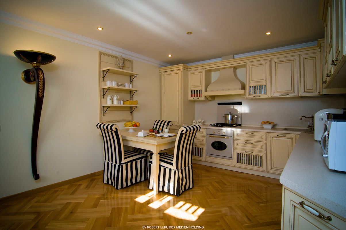 Classic white kitchen with striped chairs, parquet flooring, wooden dining table, and built-in appliances.