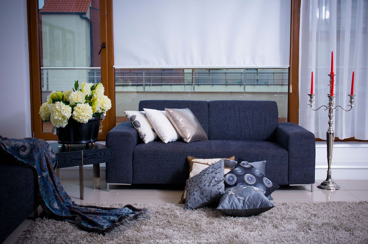 Modern navy blue sofa with decorative pillows, white hydrangeas, and red candelabra in an elegant living room.