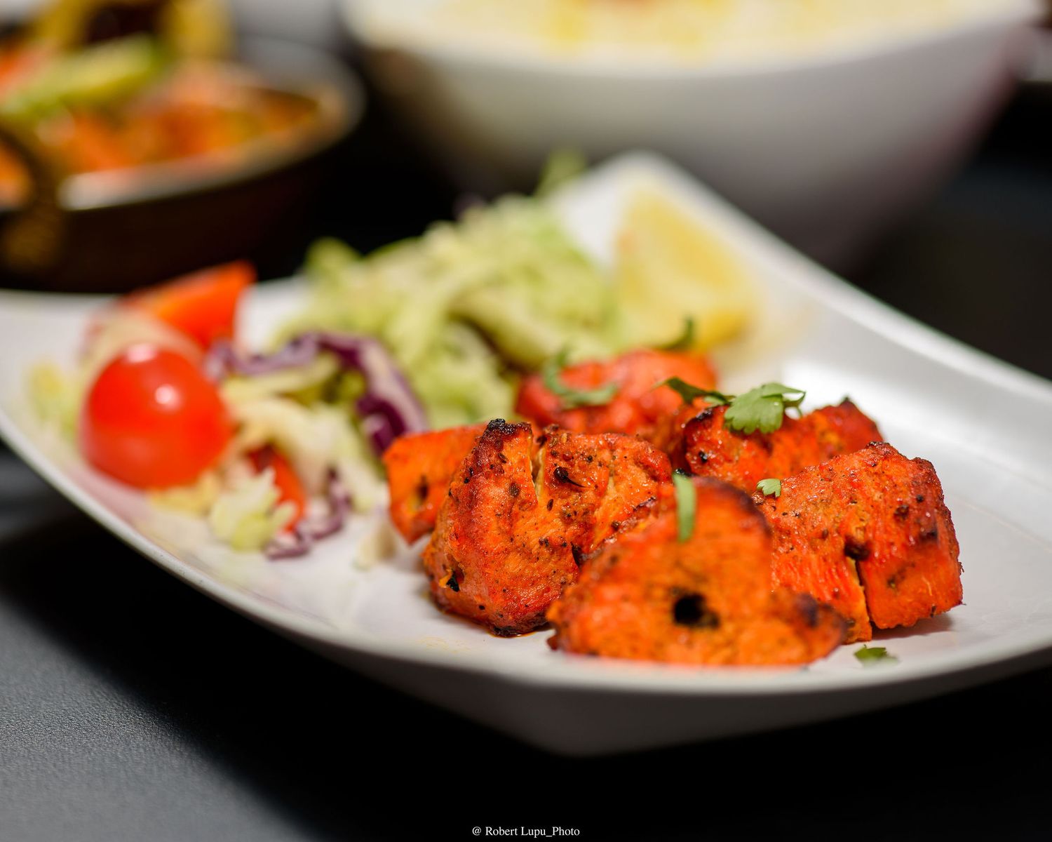 Tandoori chicken tikka served on a white plate with fresh salad, cherry tomatoes, and coleslaw at an Indian restaurant.