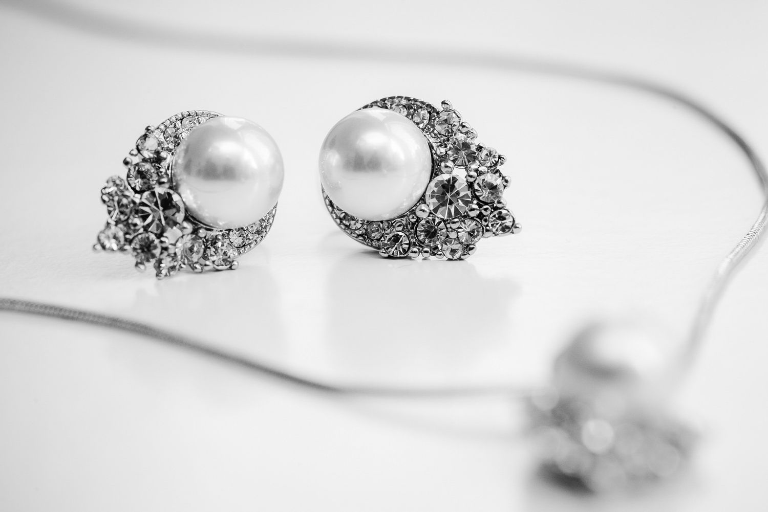 Elegant pearl and diamond cluster stud earrings in silver setting displayed on white reflective surface.