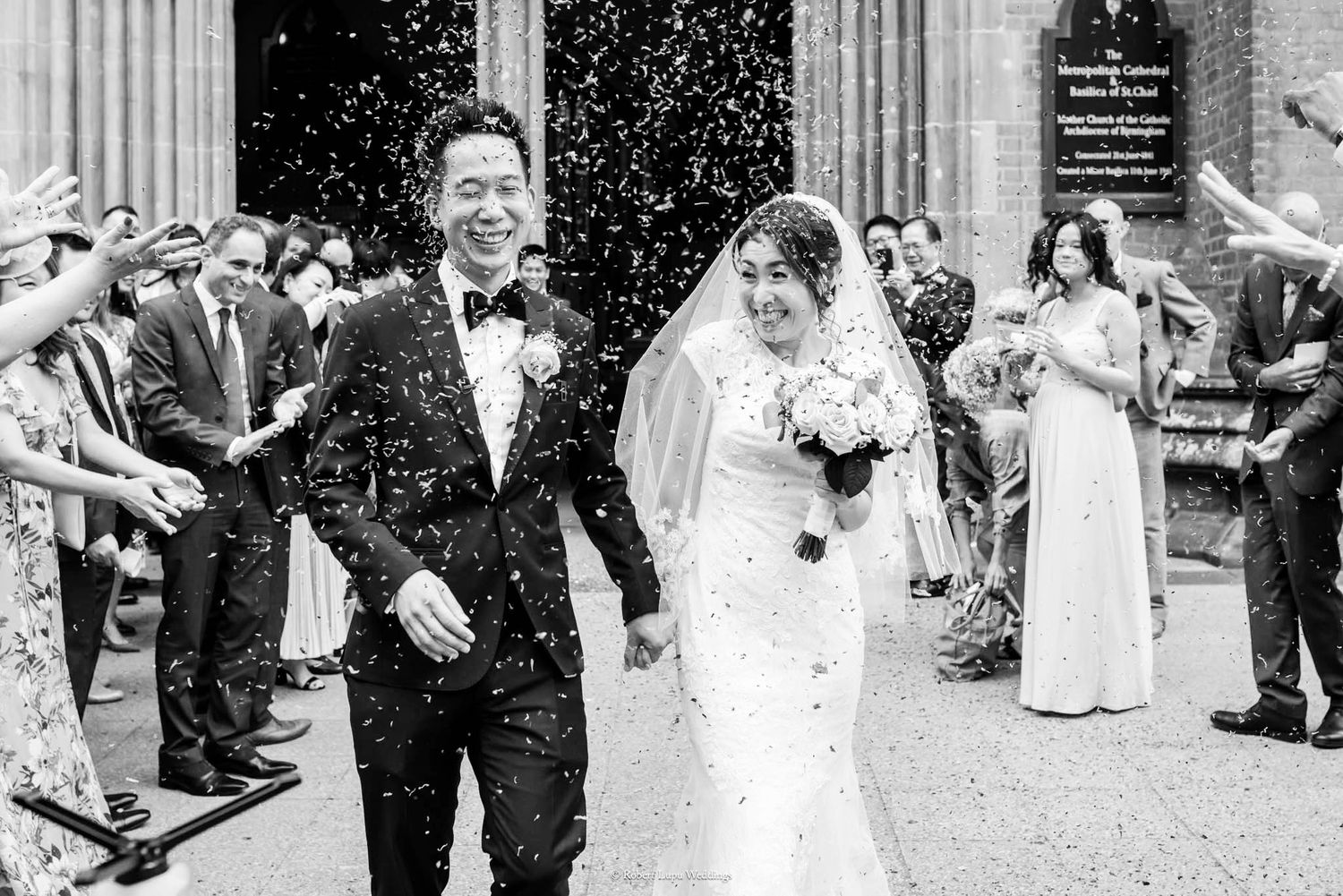 Newlywed couple walks through confetti shower outside church as guests celebrate their wedding ceremony.