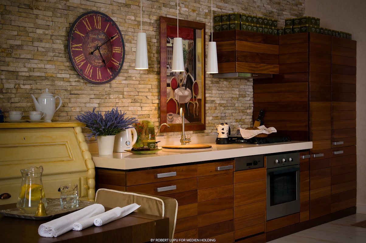 Modern kitchen with walnut wood cabinets, brick wall, vintage clock, and built-in oven in a warm, rustic setting.