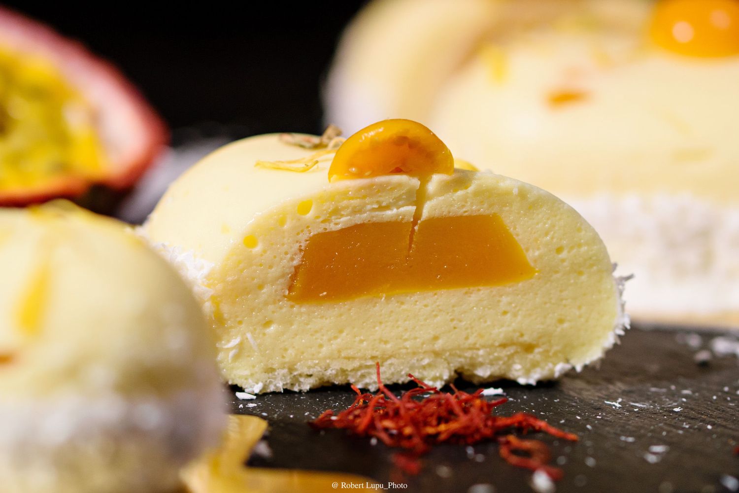 Cross-section of a creamy mochi dessert filled with passion fruit curd, garnished with saffron threads on a dark slate.