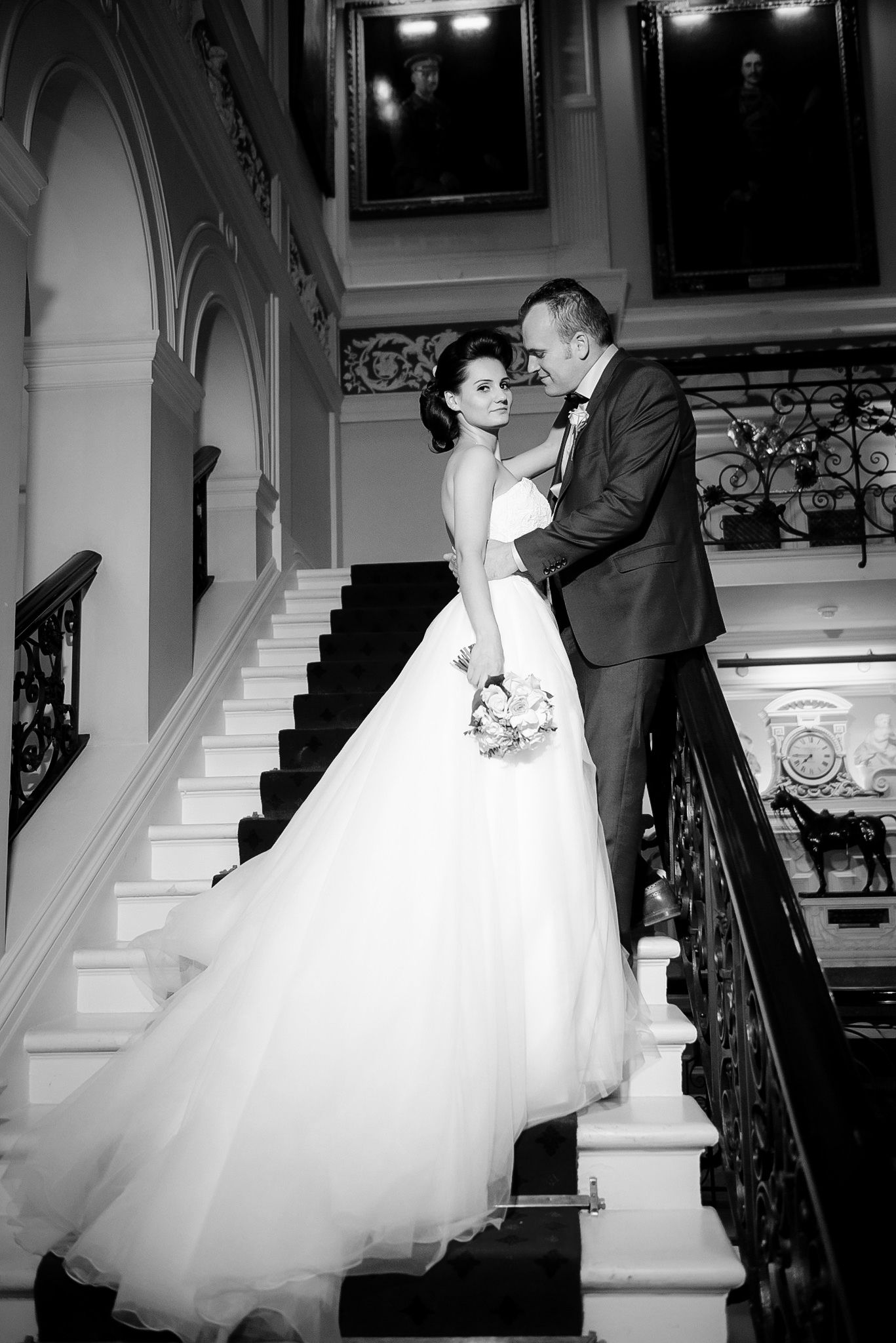 Black and white photo of bride in a full tulle gown and groom sharing a romantic moment on grand staircase.