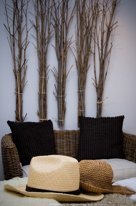 Wicker sofa with black knit pillows and straw hats, decorated with bundled bare branches.