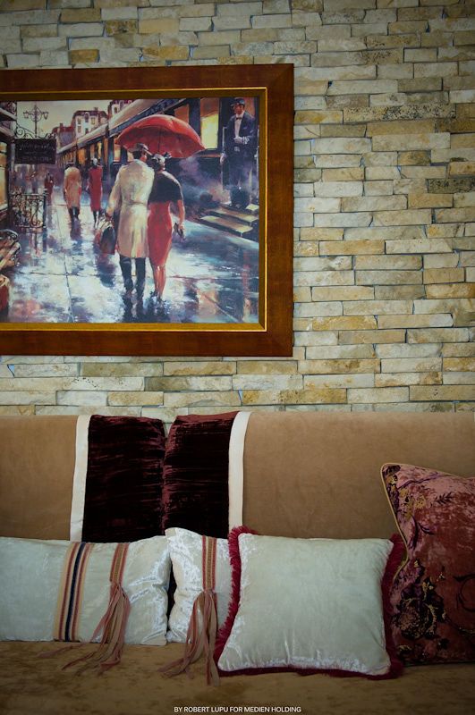 Cozy sofa with decorative pillows beneath a framed rainy street scene painting on a stone wall.
