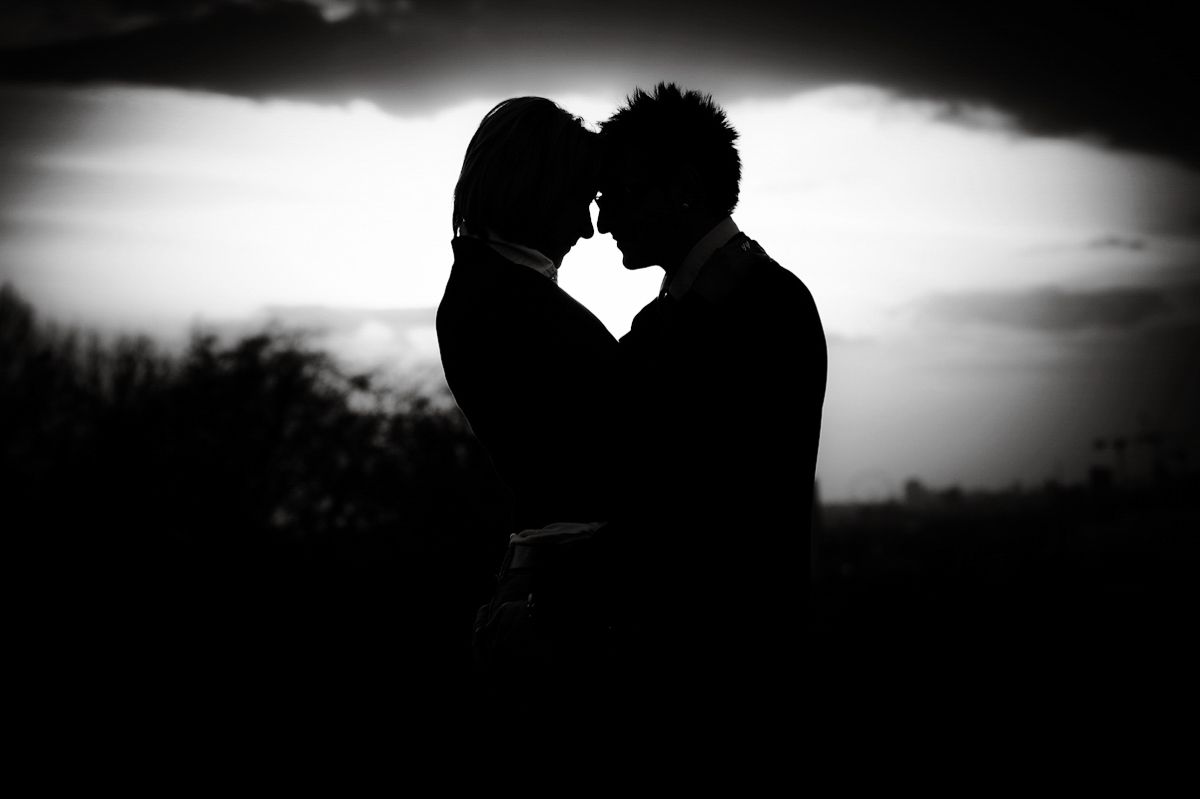 Romantic silhouette of a couple almost kissing against a dramatic cloudy sky in black and white.