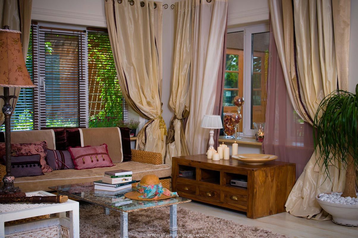 Cozy living room with flowing curtains, wooden TV stand, glass coffee table, and plush sofa with colorful pillows.