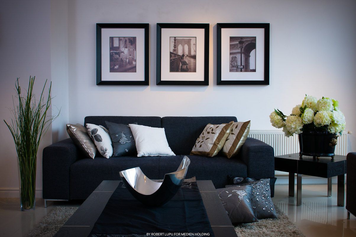 Modern living room with black sofa, decorative pillows, three framed wall art prints, and white flower arrangement on side table.