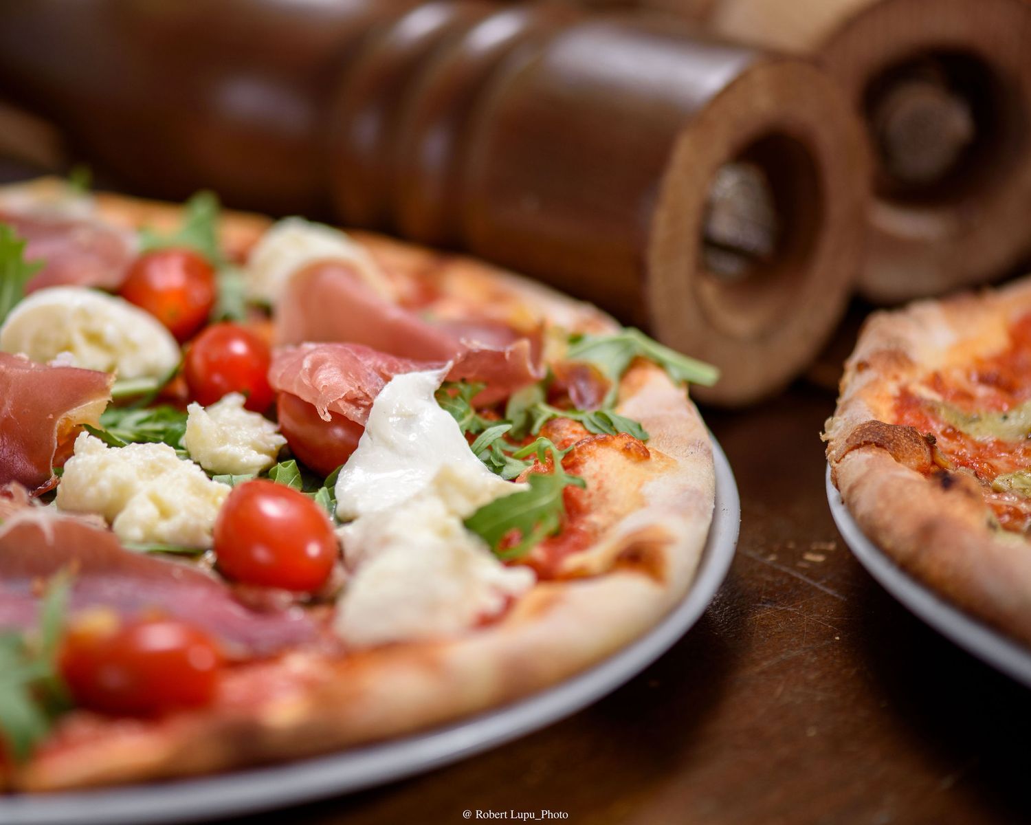 Fresh Neapolitan pizza topped with prosciutto, cherry tomatoes, mozzarella, and arugula on a rustic wooden table.