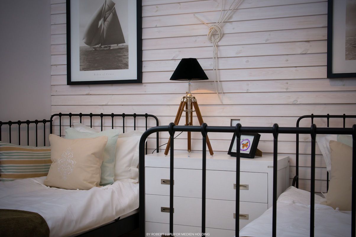 Black iron beds with white dresser, tripod lamp, and nautical framed art in a cozy coastal-themed bedroom.
