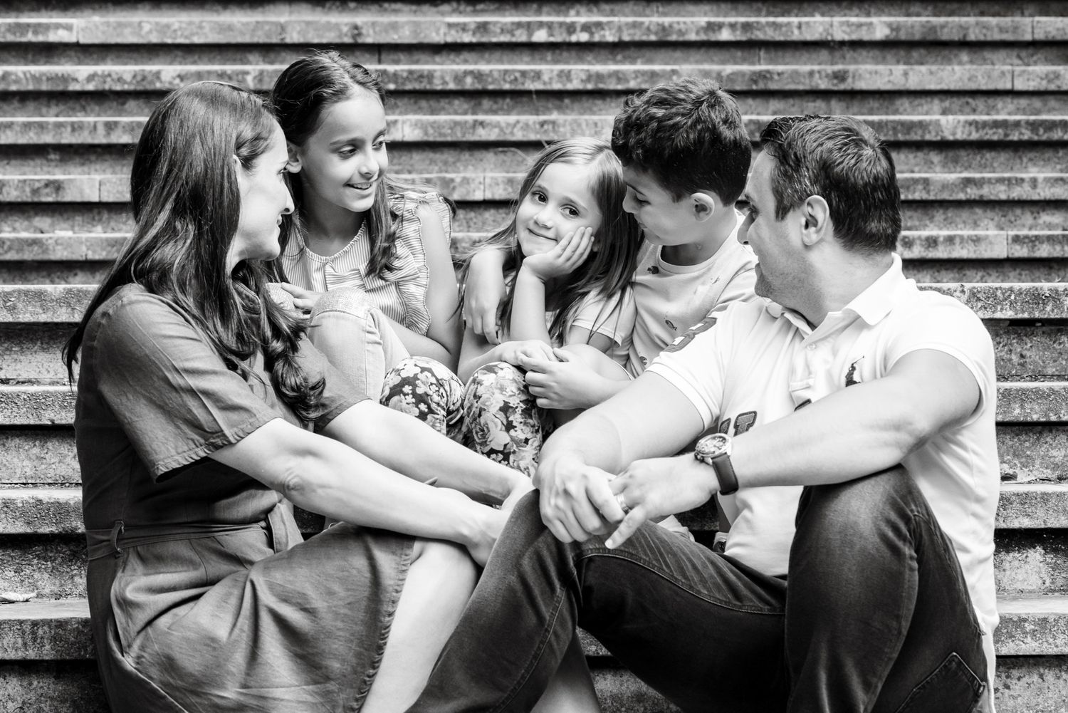 Black and white family portrait of parents and three children sitting together on stone steps, laughing and bonding.