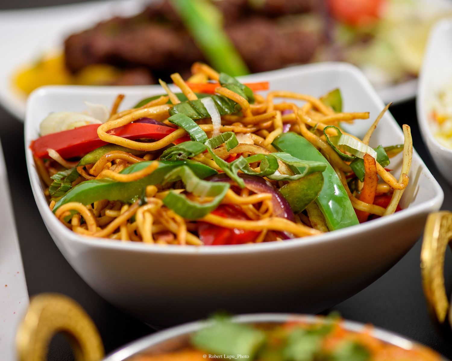 Colorful Asian noodle salad with stir-fried vegetables, snap peas, carrots, and red peppers served in a white bowl.