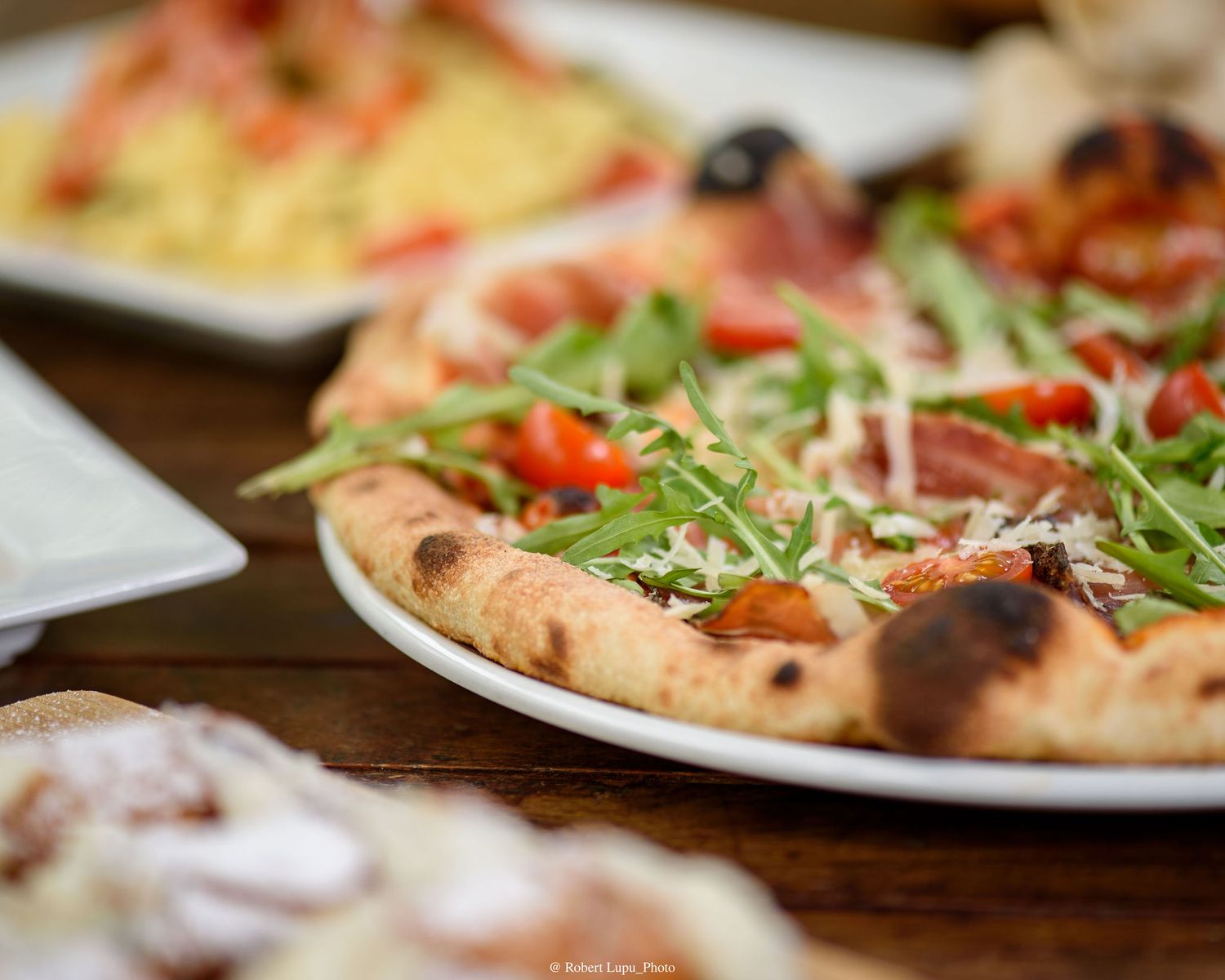 Neapolitan pizza topped with fresh arugula, cherry tomatoes, and shaved parmesan on a white plate.
