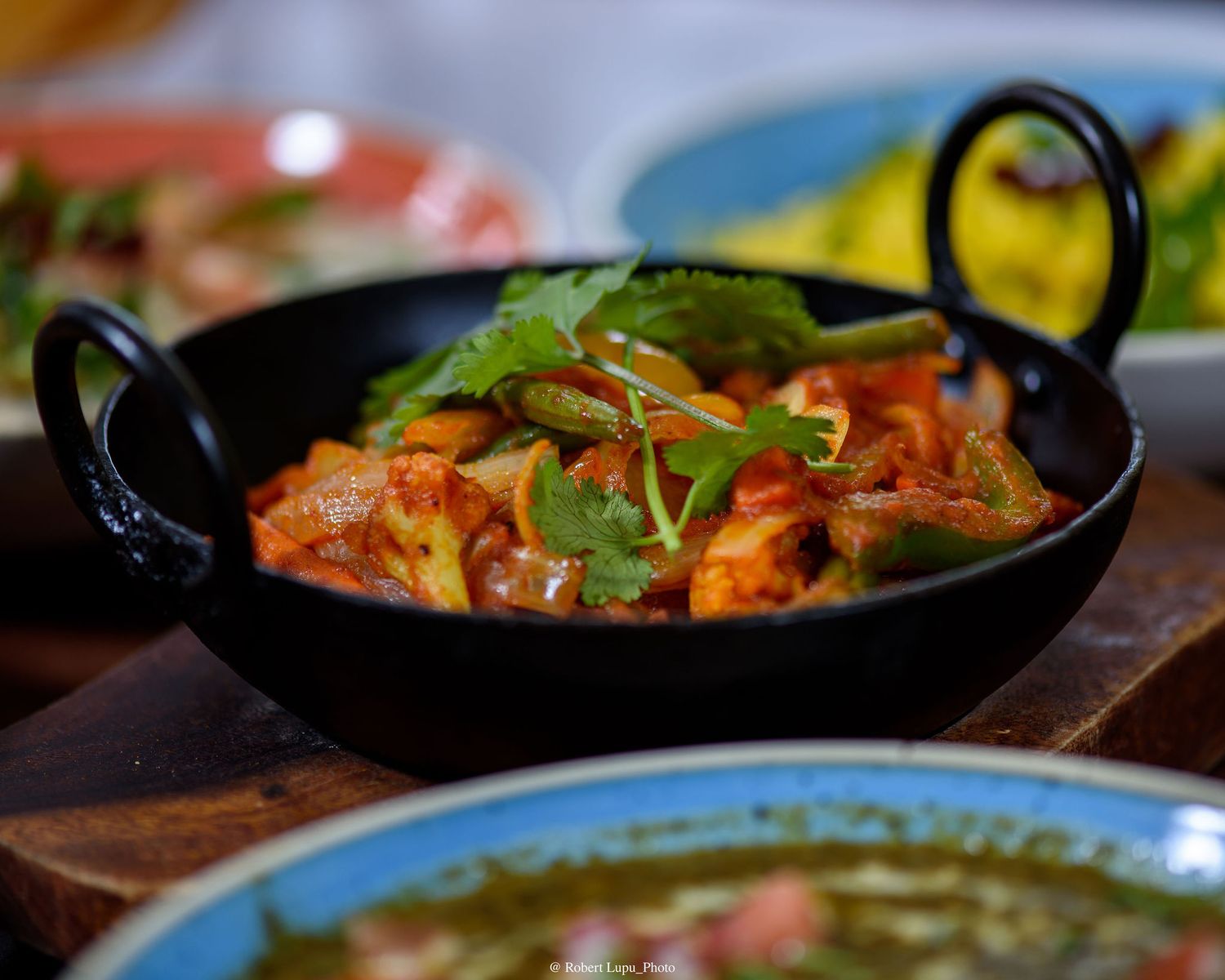Spicy Indian curry served in a black kadai pan with fresh cilantro garnish on a wooden board.