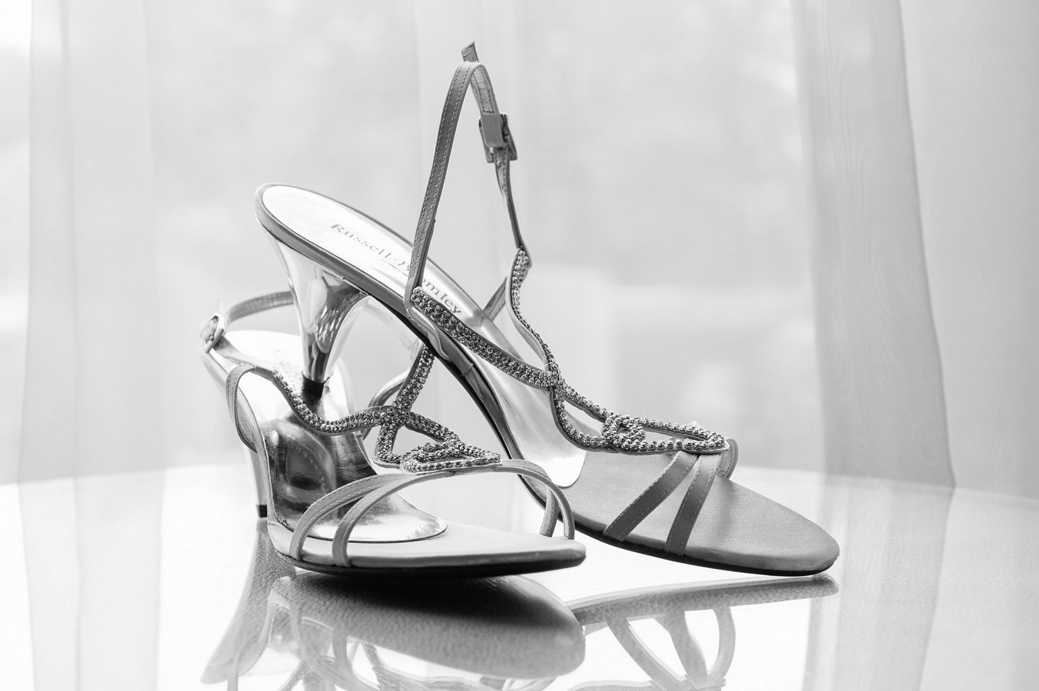 Elegant silver strappy heeled sandals with rhinestone details on a reflective surface.