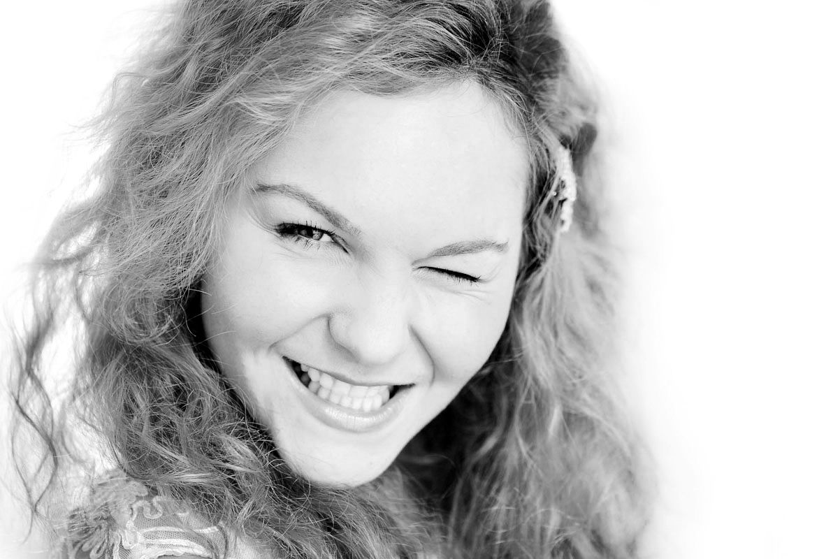 Black and white portrait of a young woman with curly hair, smiling and winking joyfully.