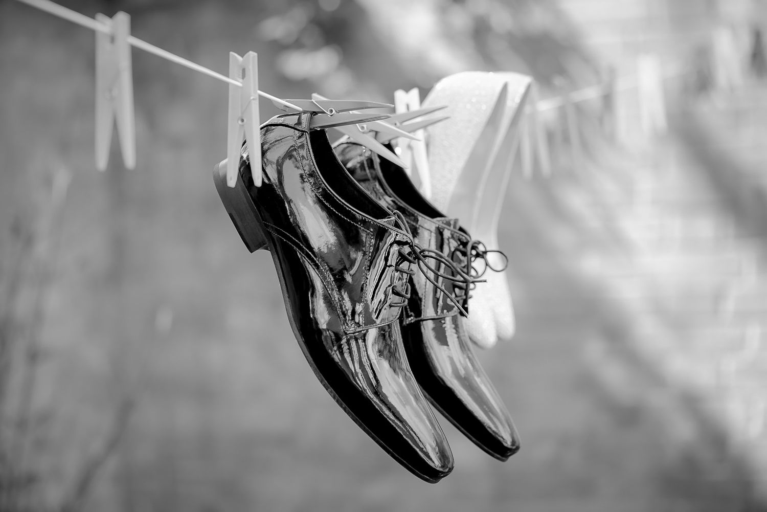 Black and white photo of polished dress shoes hanging on a clothesline secured with wooden clothespins.
