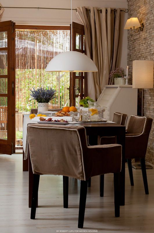 Elegant dining room with brown upholstered chairs, set table, pendant light, and open doors to garden.