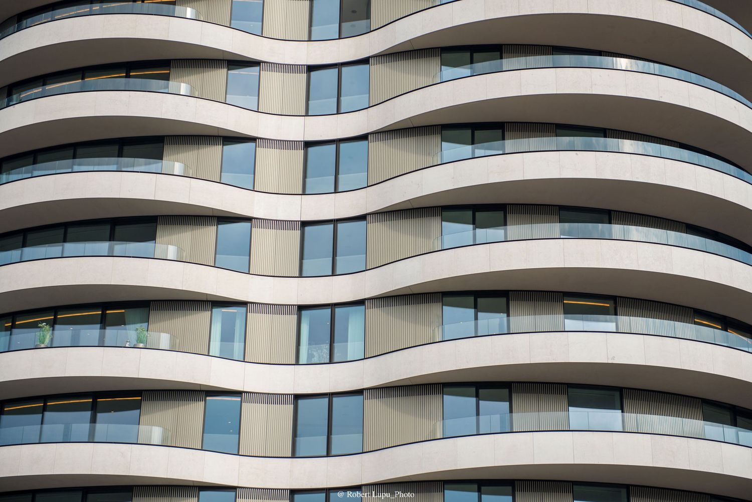 Modern curved apartment building facade with wave-shaped balconies and floor-to-ceiling windows in urban architecture.