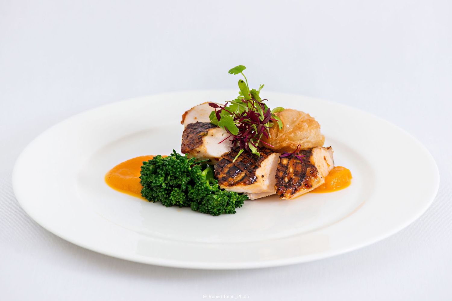 Elegant plated dish featuring seared fish, vibrant kale, orange sauce, and garnished with microgreens on a white plate.