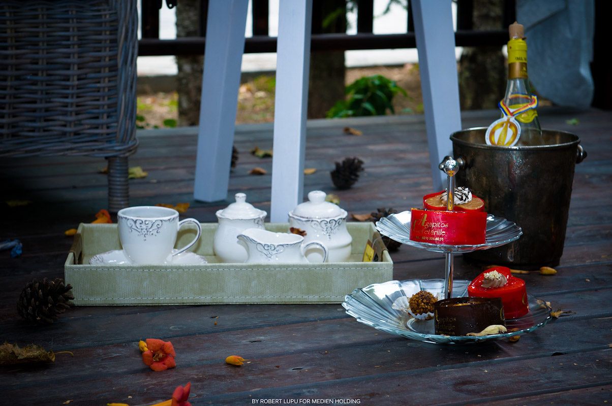 White tea set on tray with tiered cake stand and champagne bucket on rustic wooden deck.