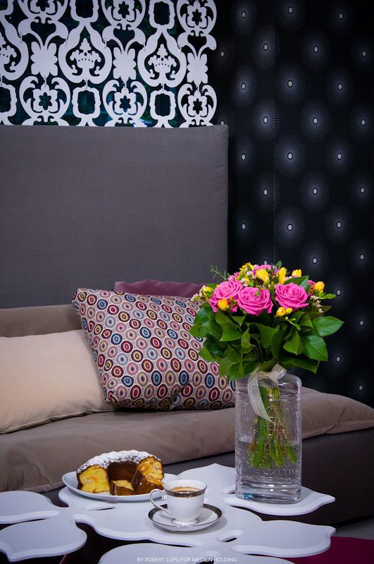 Cozy hotel lounge with pink roses bouquet, coffee cup, cake slice, and decorative pillows.